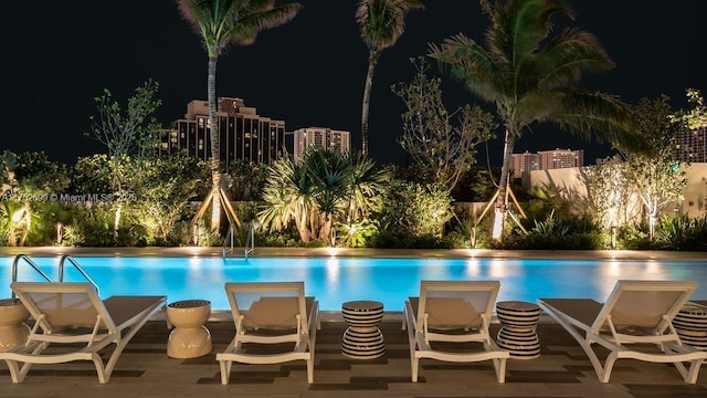 pool at night featuring an outdoor pool, a patio, and fence