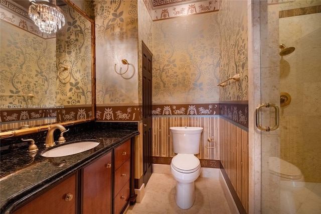 bathroom with toilet, a shower stall, wallpapered walls, baseboards, and vanity