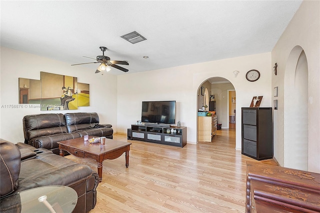 living area featuring light wood-type flooring, visible vents, arched walkways, and a ceiling fan