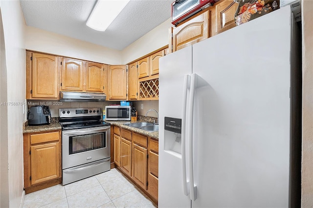 kitchen with light tile patterned floors, a sink, under cabinet range hood, a textured ceiling, and appliances with stainless steel finishes