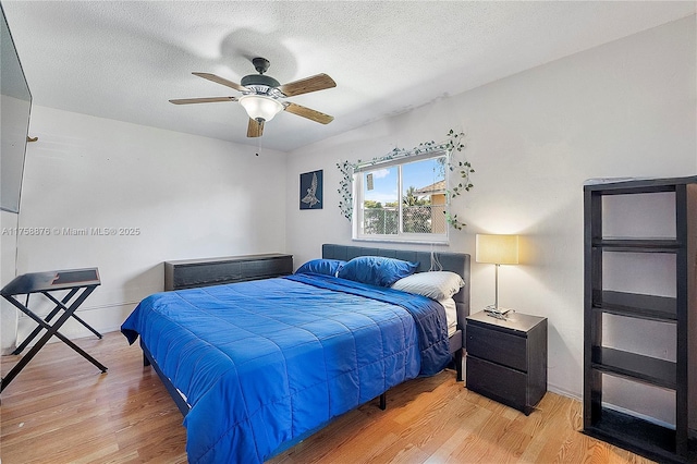 bedroom featuring baseboards, a textured ceiling, a ceiling fan, and light wood finished floors