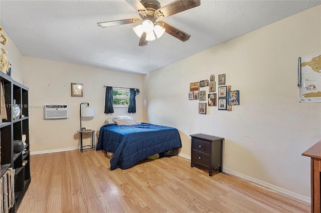 bedroom featuring a wall unit AC, a ceiling fan, baseboards, light wood-style floors, and a textured ceiling