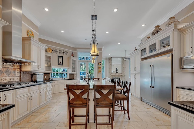 kitchen with stone tile floors, built in appliances, cream cabinets, and wall chimney range hood