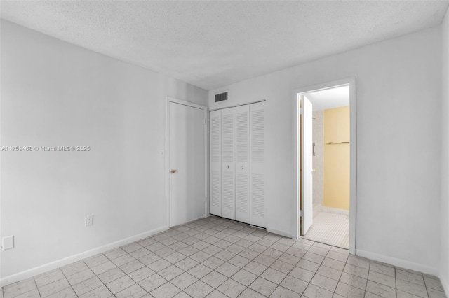 unfurnished bedroom featuring ensuite bath, visible vents, a textured ceiling, and baseboards