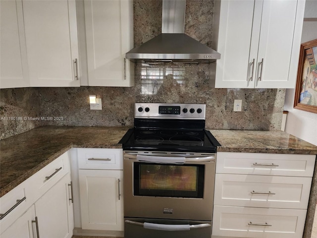 kitchen featuring dark stone countertops, tasteful backsplash, stainless steel electric range, wall chimney exhaust hood, and white cabinets