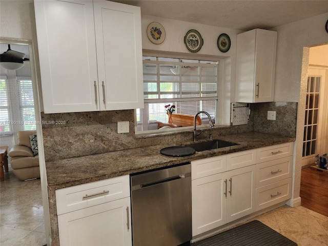 kitchen with stainless steel dishwasher, dark stone countertops, white cabinetry, and a sink