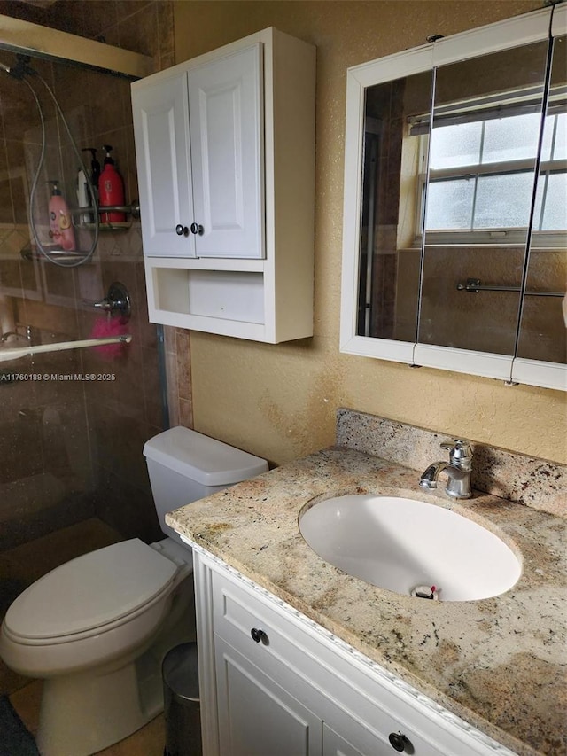 full bathroom featuring a stall shower, toilet, vanity, and a textured wall