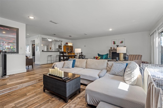 living room with light wood-type flooring, visible vents, baseboards, and recessed lighting