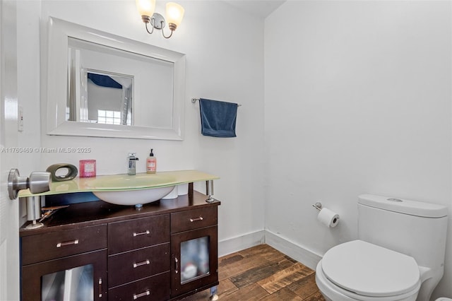 half bathroom featuring toilet, vanity, baseboards, and wood finished floors