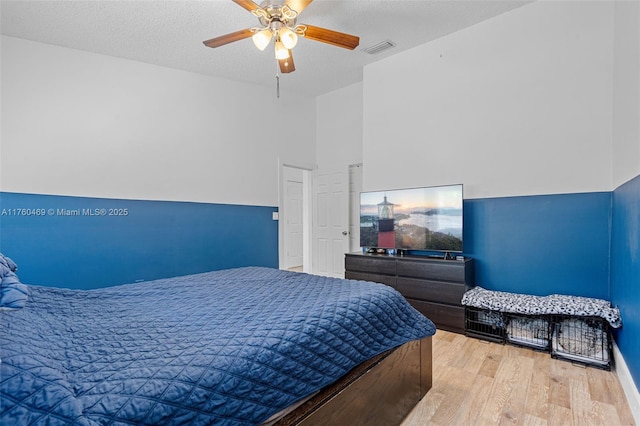 bedroom with ceiling fan, visible vents, a textured ceiling, and wood finished floors