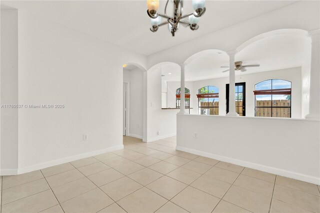 empty room with ceiling fan with notable chandelier, arched walkways, light tile patterned flooring, decorative columns, and baseboards