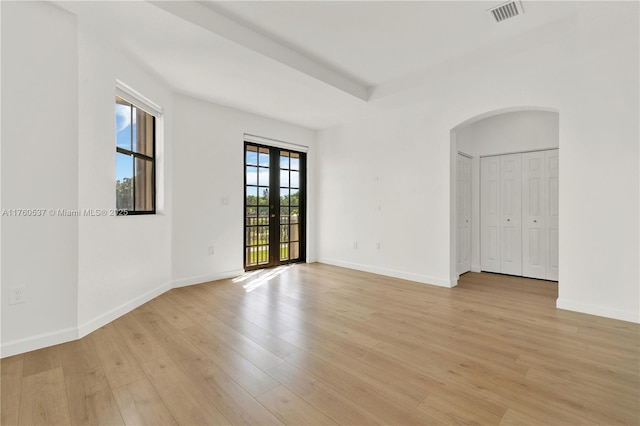 unfurnished room with visible vents, arched walkways, light wood-style flooring, and french doors