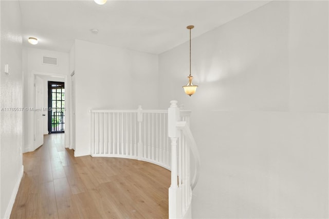 hall with light wood finished floors, visible vents, an upstairs landing, and baseboards