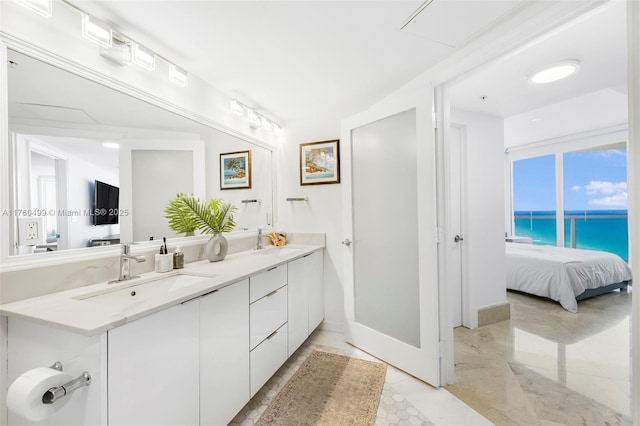 ensuite bathroom featuring double vanity, connected bathroom, a water view, and a sink
