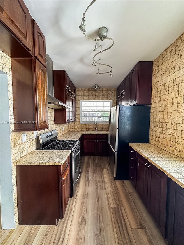 kitchen with a sink, decorative backsplash, stainless steel appliances, wall chimney exhaust hood, and light wood-type flooring