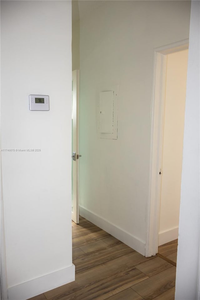 hallway with electric panel, wood finished floors, and baseboards