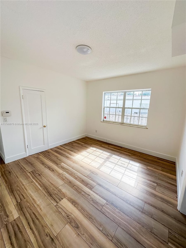 empty room featuring a textured ceiling, baseboards, and wood finished floors