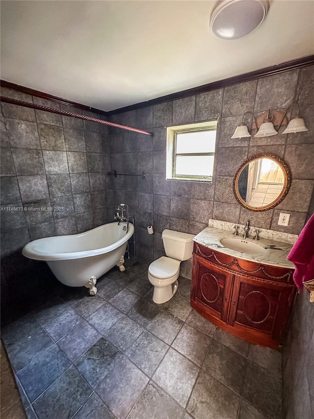 bathroom featuring tile walls, toilet, a freestanding bath, and vanity