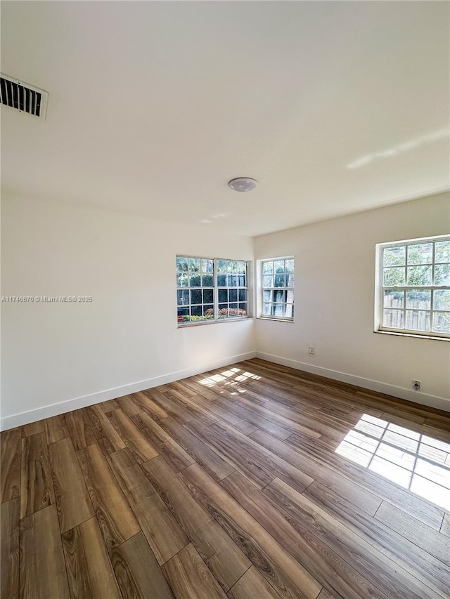 unfurnished room featuring dark wood finished floors, visible vents, and baseboards