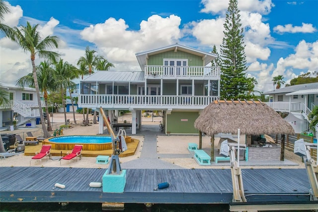 rear view of property with a balcony, a pool, a sunroom, stairs, and metal roof