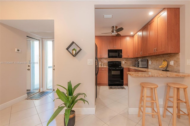 kitchen with light tile patterned floors, a breakfast bar, a peninsula, decorative backsplash, and black appliances