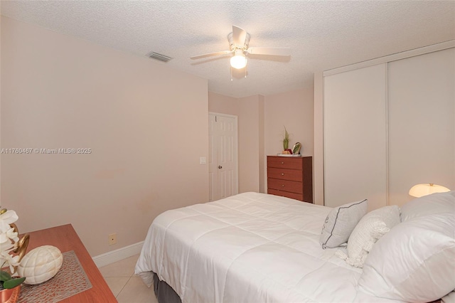 bedroom featuring visible vents, light tile patterned flooring, a closet, a textured ceiling, and a ceiling fan