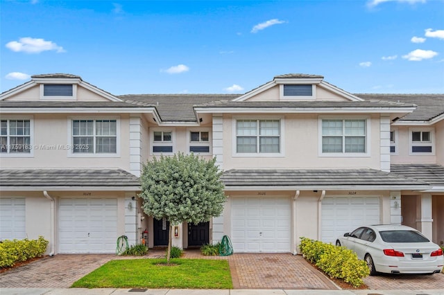 townhome / multi-family property featuring stucco siding, a garage, driveway, and a tile roof