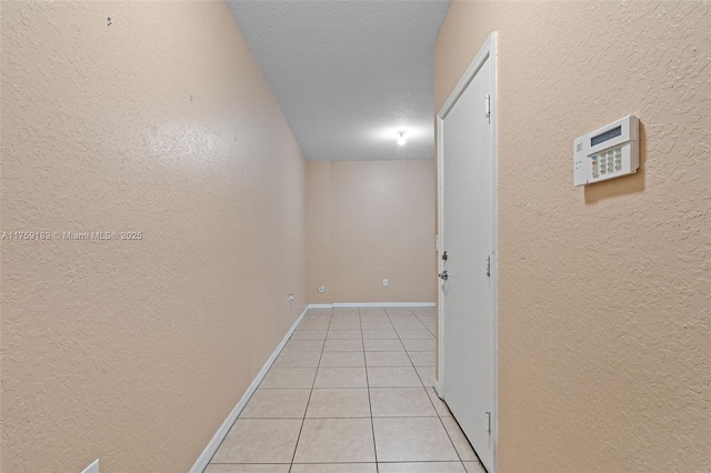 corridor featuring light tile patterned flooring, a textured wall, baseboards, and a textured ceiling