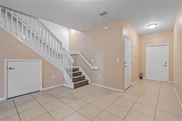 foyer with light tile patterned floors, visible vents, a textured ceiling, and stairs