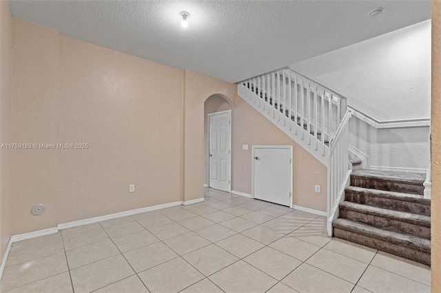 tiled spare room featuring stairway, arched walkways, a textured ceiling, and baseboards