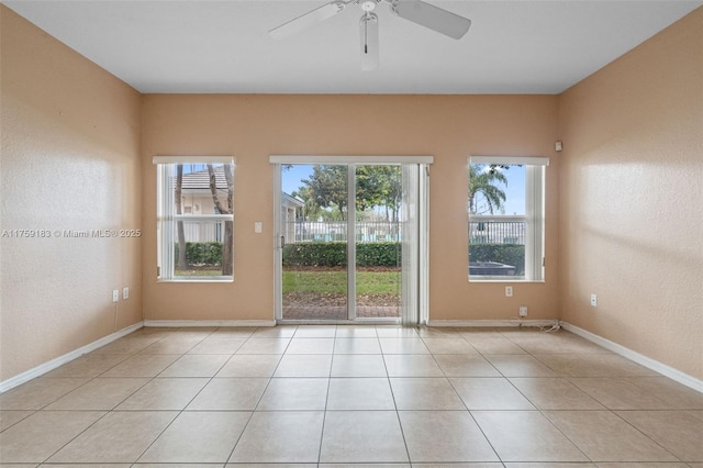 empty room with a wealth of natural light, light tile patterned floors, and baseboards