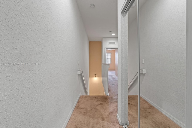 hall with visible vents, carpet flooring, a textured wall, and baseboards