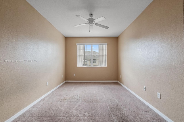 carpeted spare room with a textured wall, baseboards, and ceiling fan