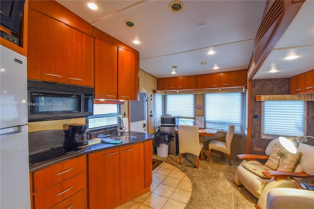 kitchen featuring light tile patterned floors, visible vents, a sink, black appliances, and dark countertops