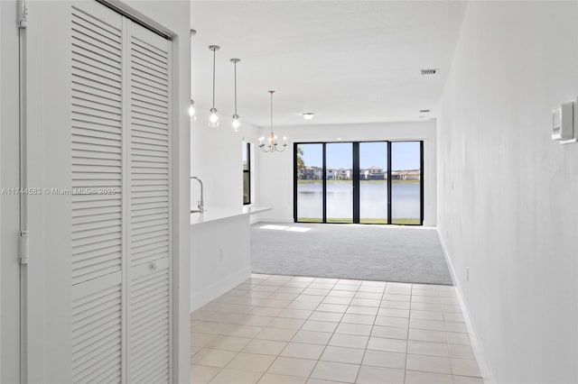 hall featuring visible vents, light carpet, a notable chandelier, a water view, and baseboards