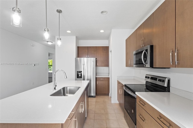 kitchen with a kitchen island with sink, a sink, stainless steel appliances, light countertops, and hanging light fixtures