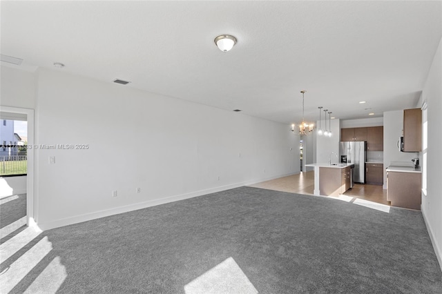 unfurnished living room featuring visible vents, baseboards, a chandelier, light carpet, and a sink