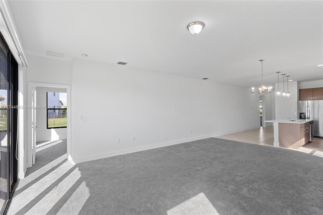 unfurnished living room featuring light carpet, a chandelier, baseboards, and a sink