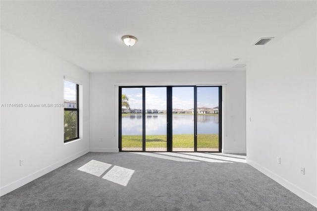 spare room featuring visible vents, carpet flooring, a healthy amount of sunlight, and a water view