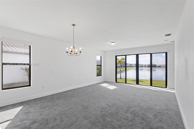 empty room with visible vents, baseboards, carpet, a water view, and an inviting chandelier