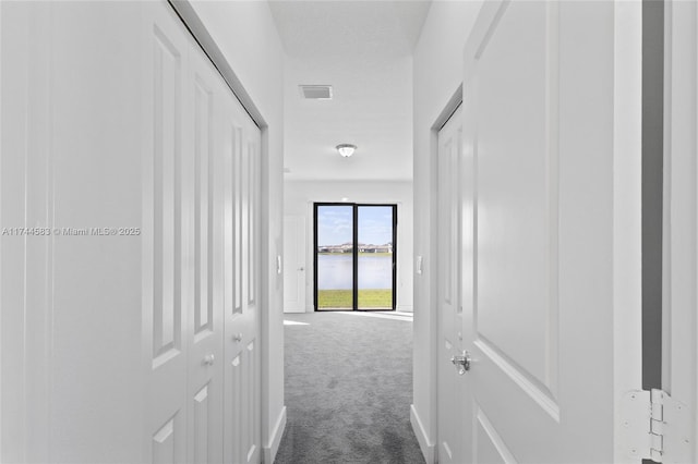 corridor featuring visible vents, a water view, and dark colored carpet