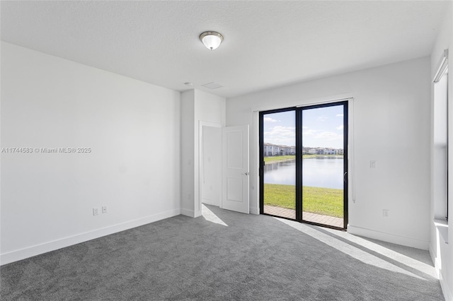 carpeted spare room featuring baseboards, a water view, and a textured ceiling