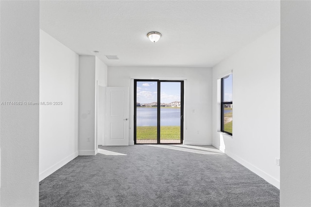 carpeted spare room with baseboards, visible vents, and a water view