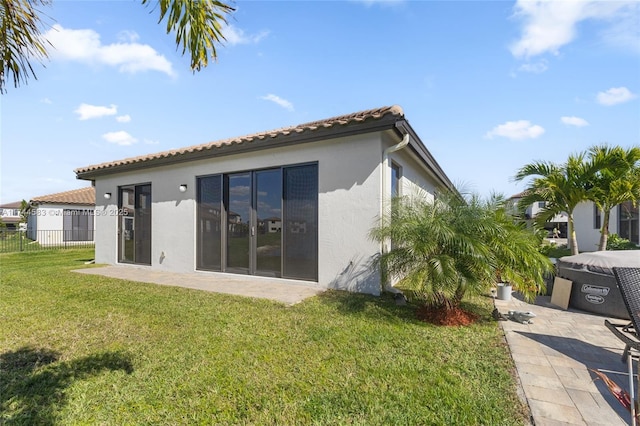 rear view of property featuring fence, a tile roof, a lawn, stucco siding, and a patio area