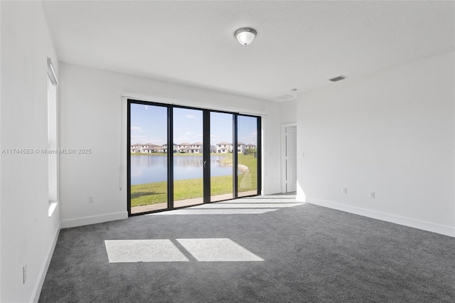 empty room featuring visible vents, baseboards, carpet, and a water view