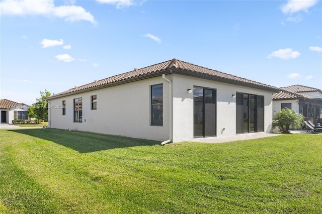 back of property featuring stucco siding, a lawn, and a tile roof