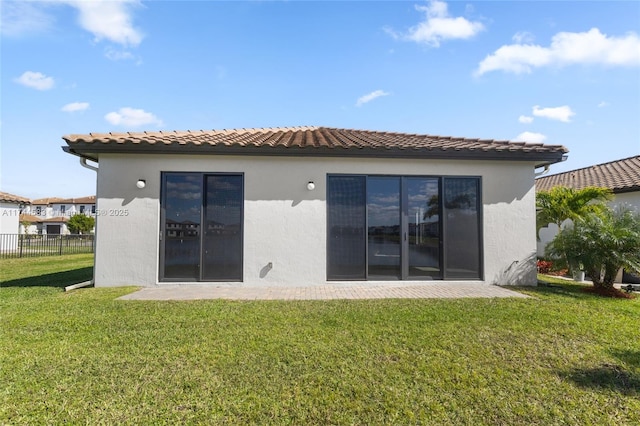 back of property featuring stucco siding, a lawn, a tiled roof, and fence