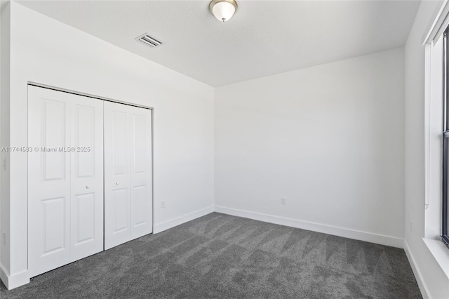 unfurnished bedroom featuring a closet, visible vents, baseboards, and dark colored carpet