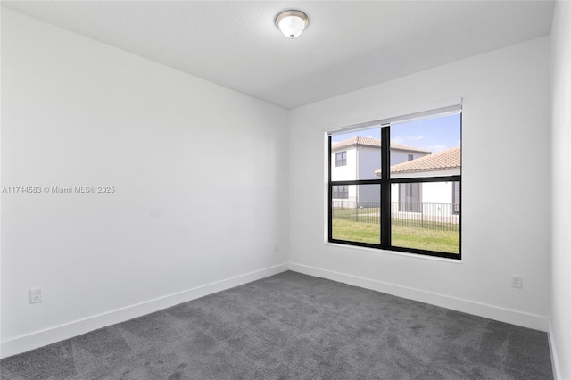 unfurnished room with baseboards and dark carpet