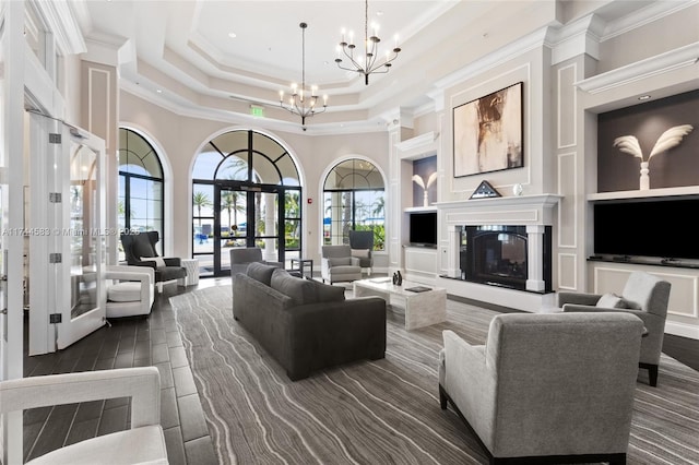 living area with built in shelves, a notable chandelier, a tray ceiling, a glass covered fireplace, and crown molding